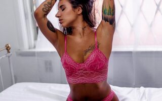 Woman Wearing Pink Lingerie Kneeling on Top of Bed While Tying Hair