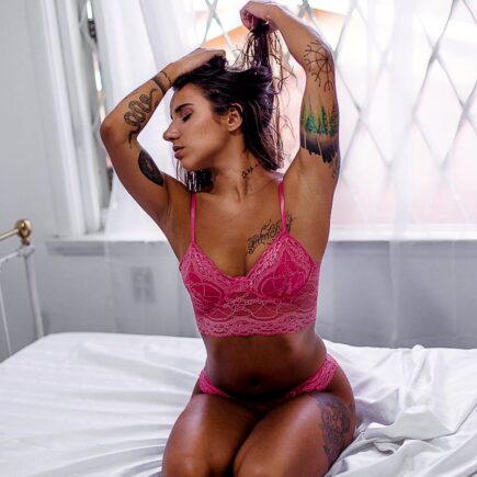 Woman Wearing Pink Lingerie Kneeling on Top of Bed While Tying Hair