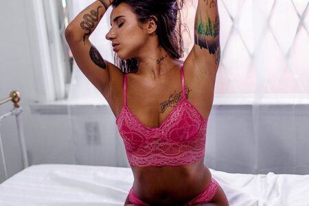 Woman Wearing Pink Lingerie Kneeling on Top of Bed While Tying Hair