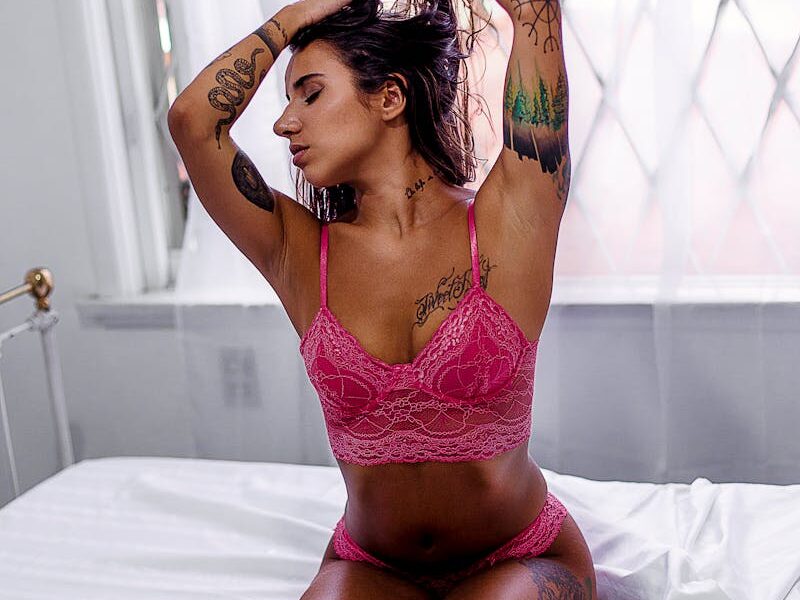 Woman Wearing Pink Lingerie Kneeling on Top of Bed While Tying Hair